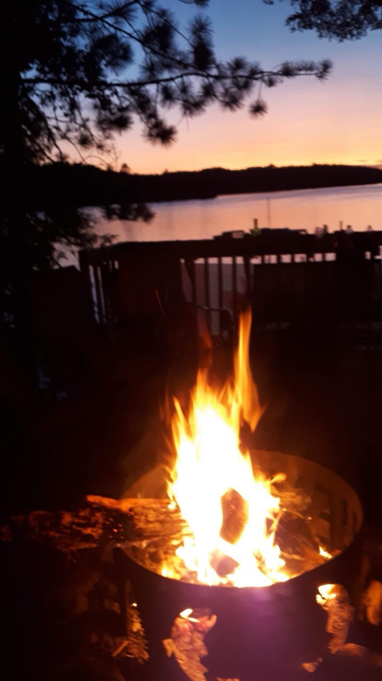A fire burning in a backyard fire pit at sunset beside the water