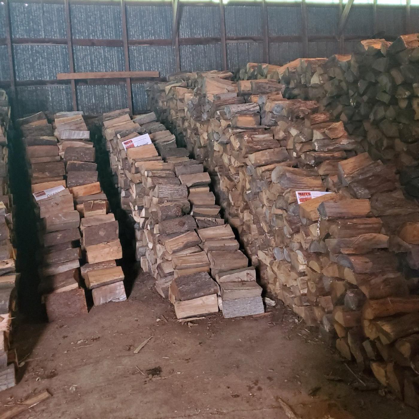 Rows of split hardwood stacked and seasoning inside a barn